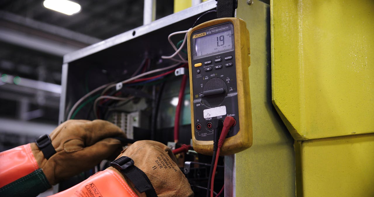 creative Electrician using a multimeter to fix industrial control panel wiring.