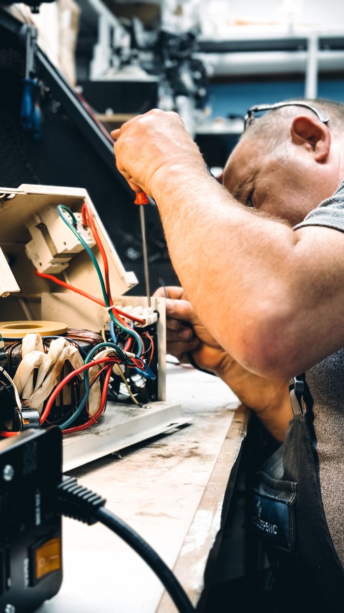 Services-02 Expert electrician repairing an electrical device in a workshop setting, focusing on wiring.