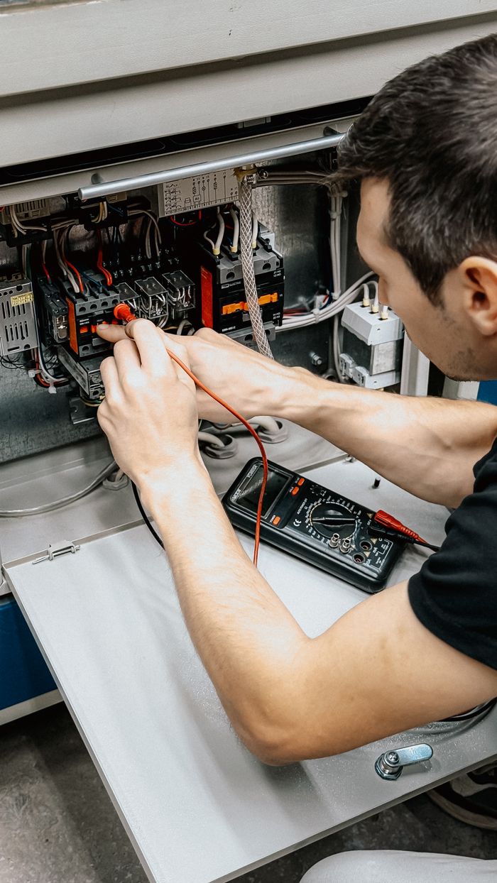 why-choose-us An electrician uses a multimeter to test and diagnose connections in an open electrical panel.