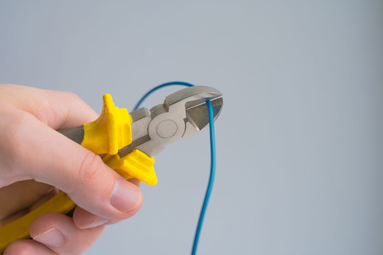 Detailed image of a hand using pliers to cut a blue wire on a gray background.