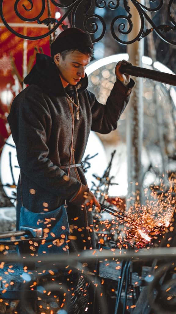 Chi Siamo A skilled blacksmith crafting metal with sparks flying in an artistic workshop setting.
