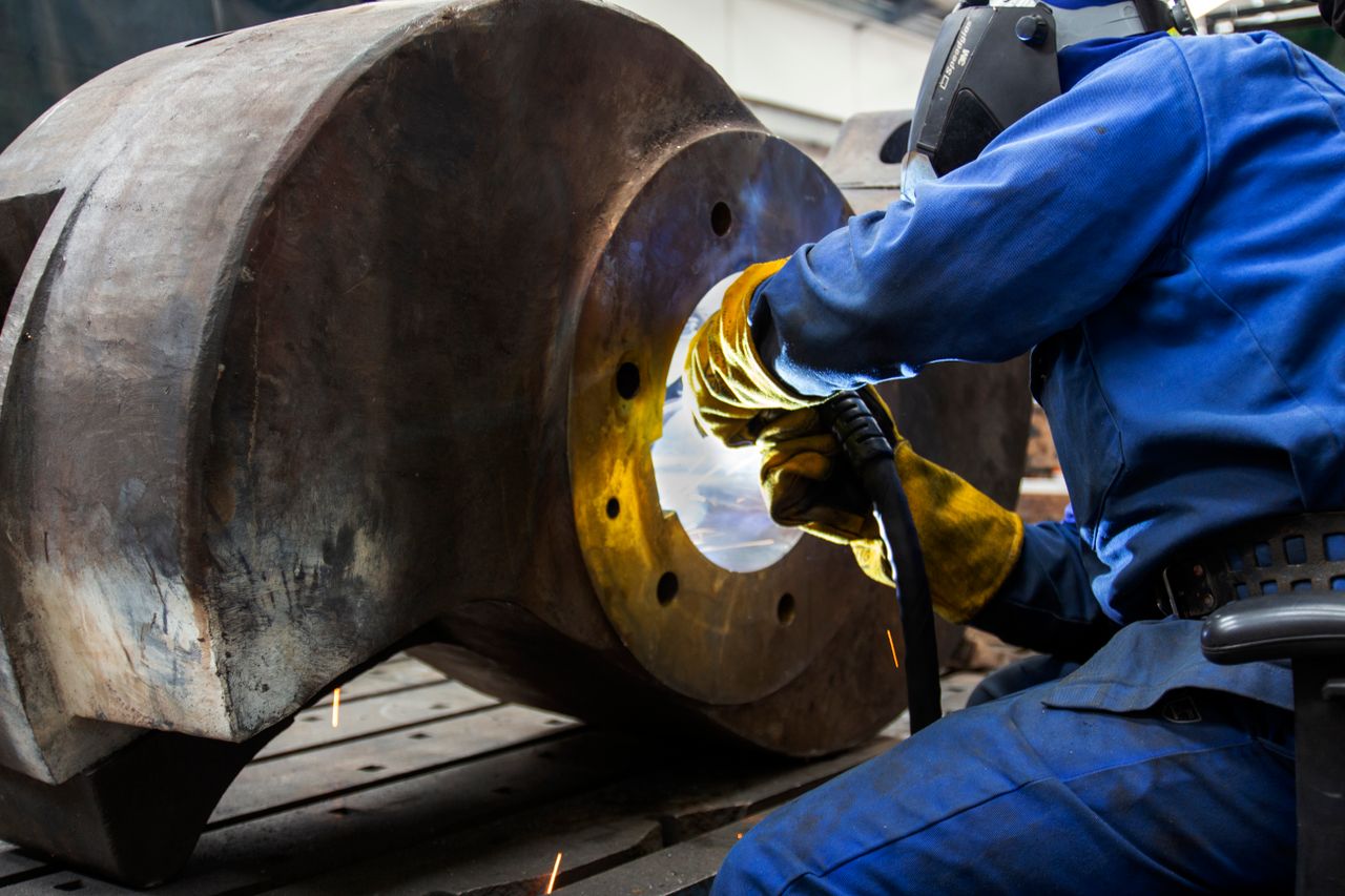 team-05 A welder wearing safety gear operates on a large metal component in an industrial setting.