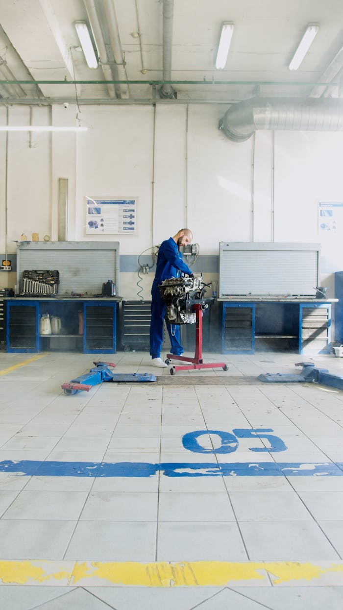 gallery-6 A mechanic in blue overalls repairs an engine in a spacious, well-lit garage.