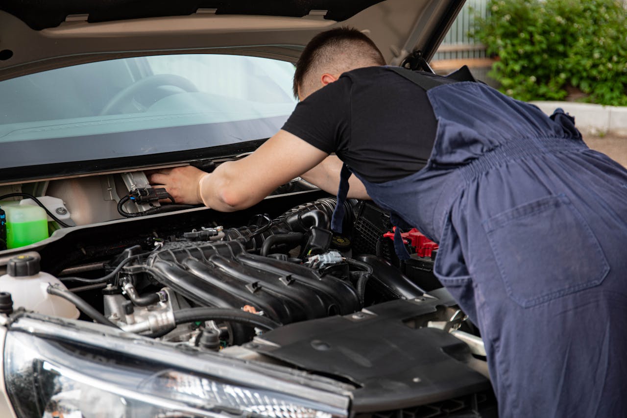 about-01 A mechanic performing maintenance work on a cars engine in an outdoor setting.