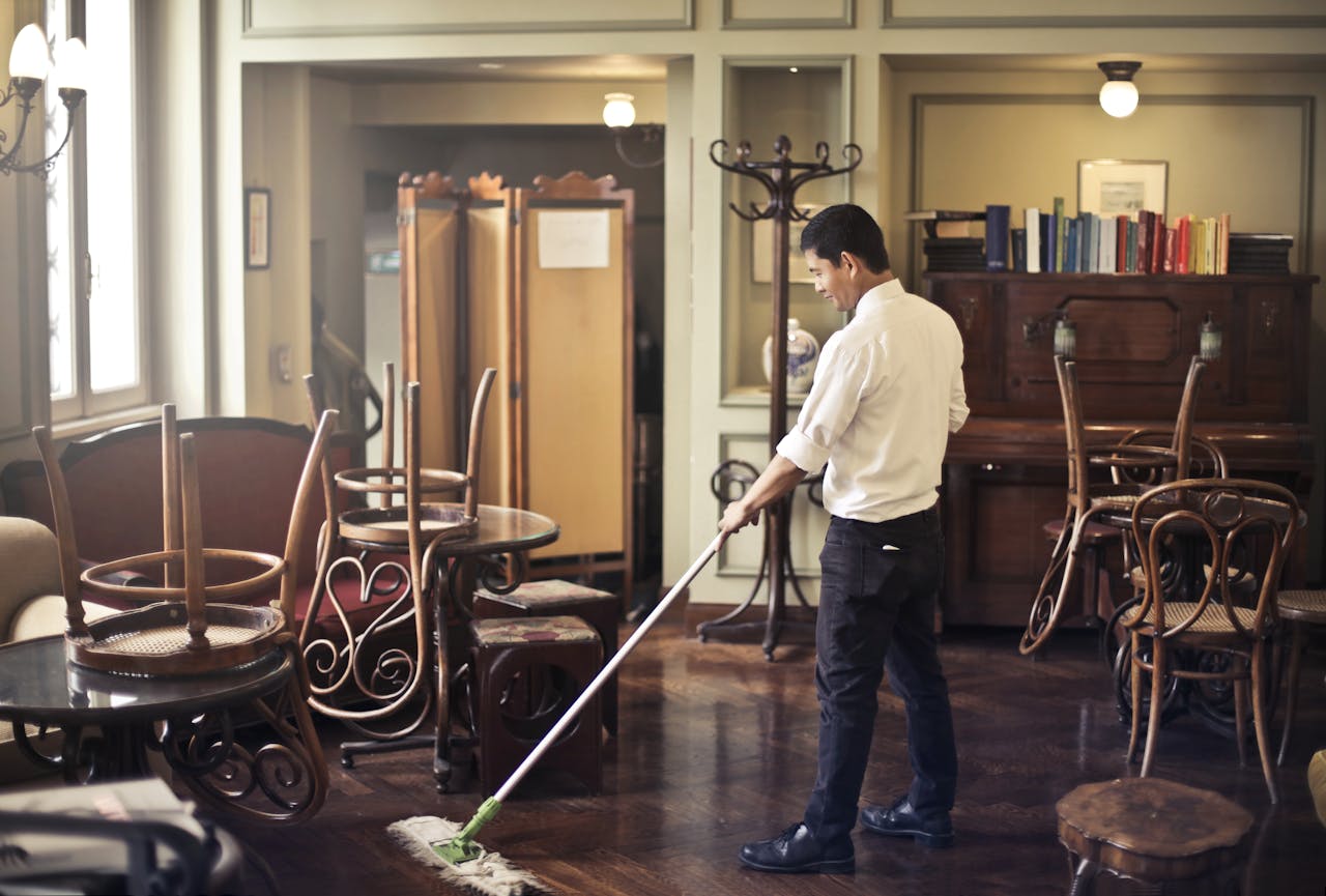 home-hero Side view of young ethnic male in uniform cleaning floor with mop while working in retro styled restaurant