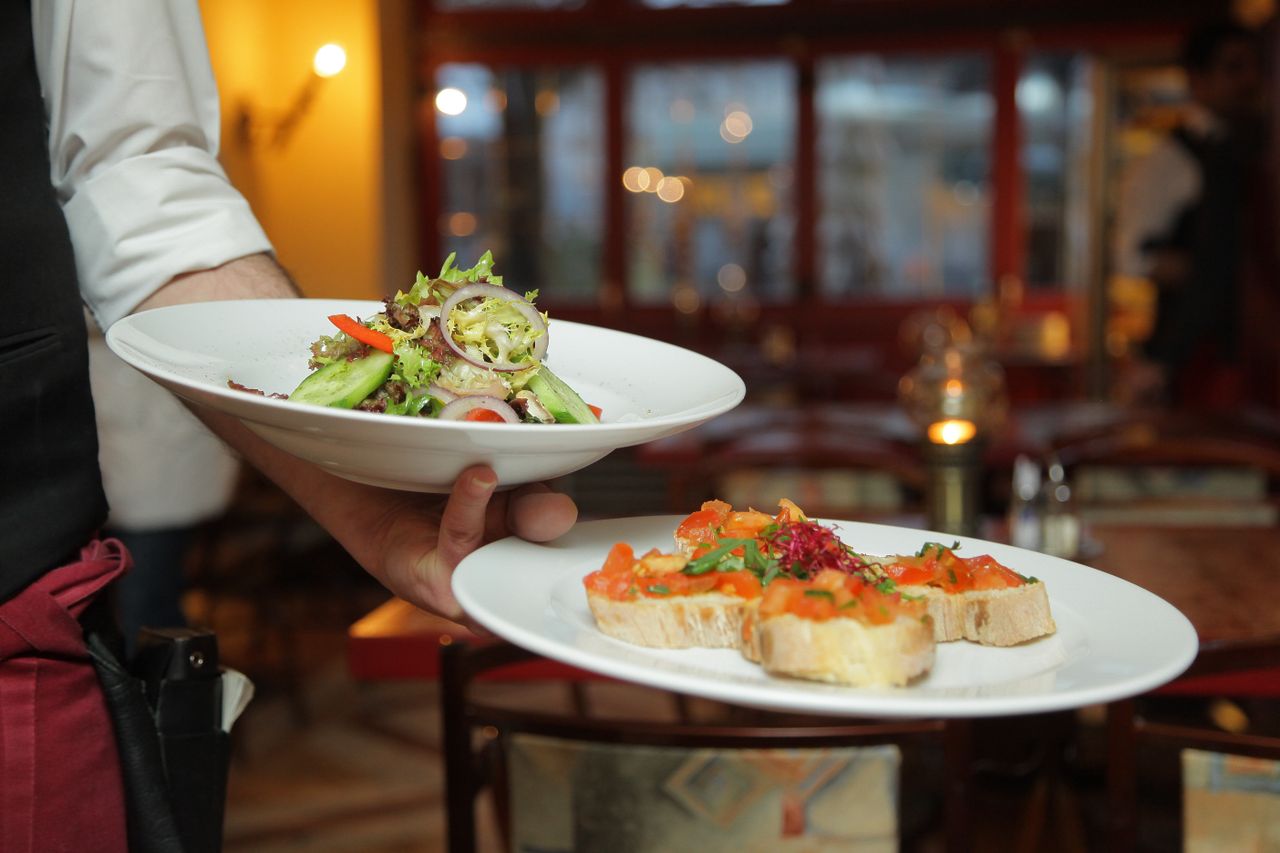 about-03 A waiter serves a fresh salad and hors doeuvres in a cozy restaurant setting.