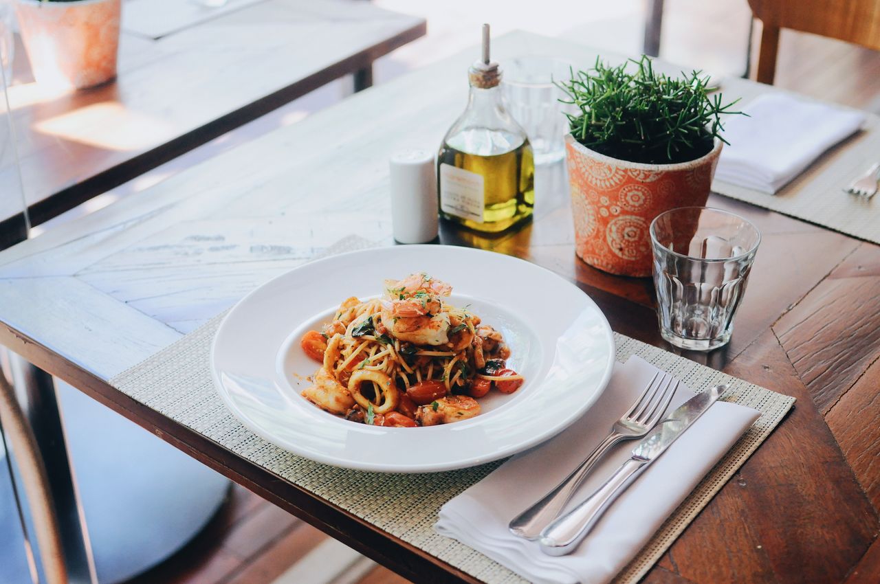 about-04 A delectable seafood pasta dish with olive oil and fresh herbs on a restaurant table setting.